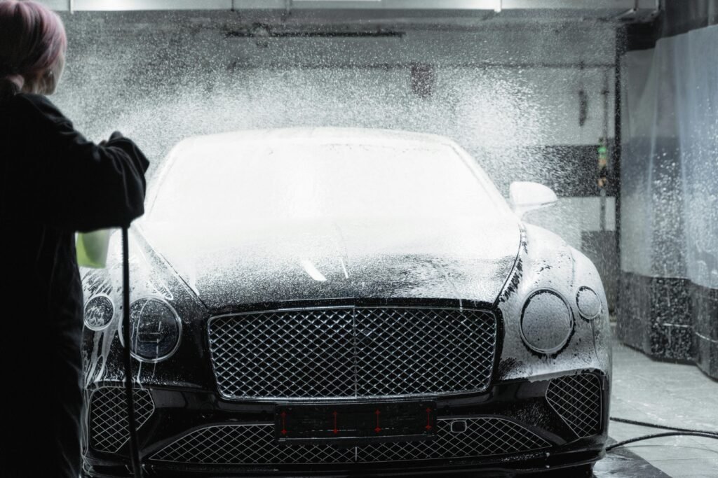Black luxury car receiving a foamy wash in an indoor car wash service.